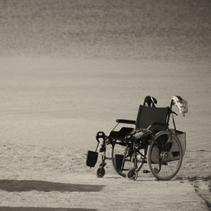 Ein leerer Rollstuhl und ein Gehstock auf einem Sandboden vermitteln ein Gefühl von Abwesenheit oder Abschied.