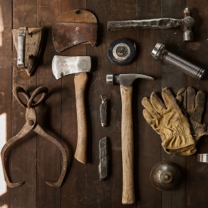 Verschiedene alte Werkzeuge, darunter Hämmer, eine Axt, Handschuhe und Scheren, ordentlich auf einer Holzoberfläche angeordnet.