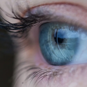 Nahaufnahme eines menschlichen Auges mit detaillierter blauer Iris, Wimpern und umgebender Haut.