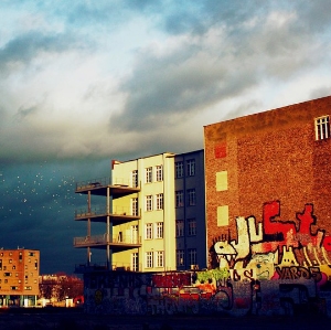 Eine Stadtlandschaft mit Graffiti bedeckten Gebäuden und einem stürmischen Himmel, das Sonnenlicht wirft dramatische Schatten.
