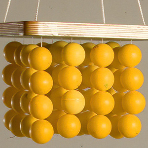 Ein quadratischer Abakus mit vier hängenden Stäben, jeder mit mehreren gelben Perlen versehen, vor einem einfarbigen Hintergrund.