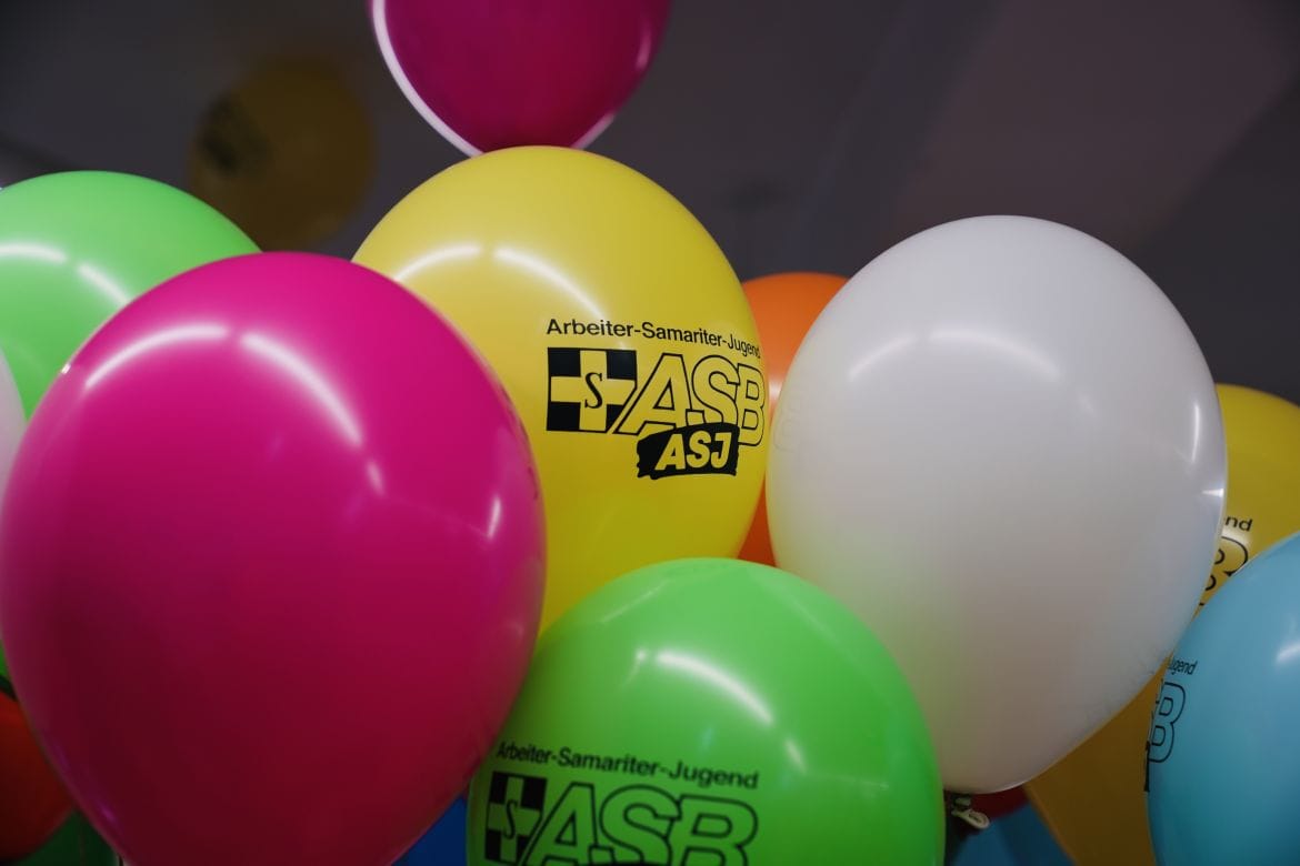 Nahaufnahme von bunten Luftballons mit dem Schriftzug „Arbeiter-Samariter-Jugend ASJ“ in einem Raum.