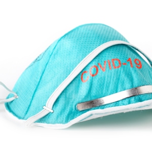 Eine blaue medizinische Gesichtsmaske mit der Aufschrift „Covid-19“, mit einem verstellbaren Nasenstreifen aus Metall und elastischen Bändern, isoliert auf weißem Hintergrund.