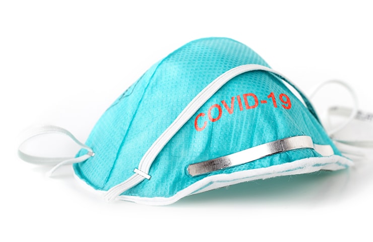 Eine blaue medizinische Gesichtsmaske mit der Aufschrift „Covid-19“, mit einem verstellbaren Nasenstreifen aus Metall und elastischen Bändern, isoliert auf weißem Hintergrund.