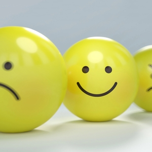 Vier gelbe Emoticon-Bälle zeigen vor einem sanften grauen Hintergrund unterschiedliche Emotionen von Traurigkeit und Wut bis hin zu Freude.