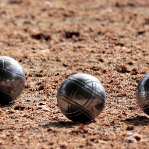 Drei metallene Pétanque-Kugeln und eine kleine hölzerne Zielkugel auf einem Sandplatz.