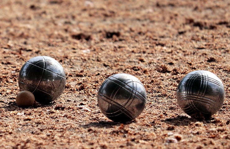 Drei metallene Pétanque-Kugeln und eine kleine hölzerne Zielkugel auf einem Sandplatz.