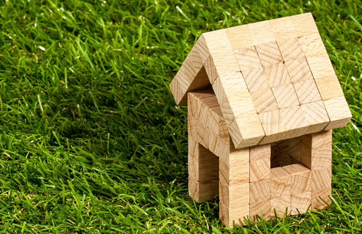 Ein kleines Haus aus Holzklötzen, das auf einer Grasfläche aufgebaut ist.