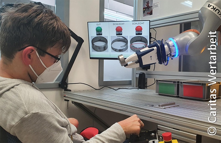 Eine Person mit Maske arbeitet an einer Laborstation mit einem Roboterarm und einem Monitor, auf dem die Ergebnisse der Qualitätskontrolle angezeigt werden.