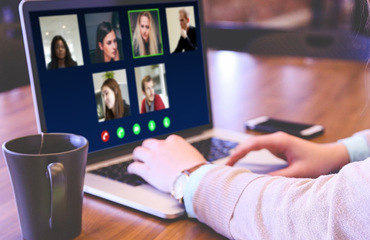 Eine Frau mit einer Armbanduhr nimmt an einem Videoanruf auf ihrem Laptop teil. Auf dem Display sind vier weitere Teilnehmer zu sehen. In der Nähe steht eine Kaffeetasse.