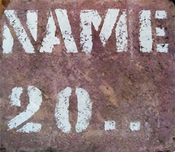 Schablonengraffiti auf einer verwitterten Oberfläche, das das Wort „Native“ über der Zahl „20“ zeigt.