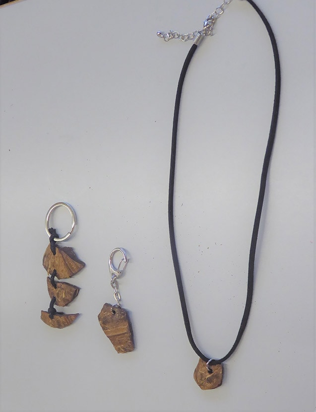 Zwei Schlüsselanhänger mit Holzanhänger und eine schwarze Kordelkette mit einem ähnlichen Holzanhänger auf hellgrauem Hintergrund.