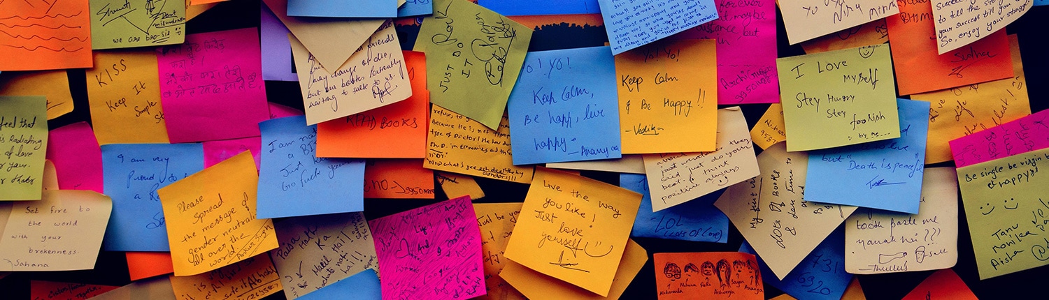 Seitenbild-Pinnwand: Eine Wand voller bunter Haftnotizen. Jede Notiz enthält verschiedene handschriftliche Nachrichten, von Erinnerungen bis hin zu motivierenden Zitaten. Die Haftnotizen sind in verschiedenen Farben, darunter Blau, Gelb, Rosa und Orange, und überlappen sich.