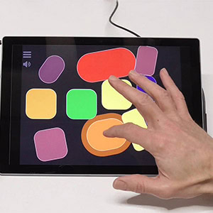 Eine Hand interagiert mit farbigen geometrischen Formen auf einem Tablet-Bildschirm.