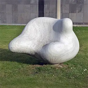 Glatte, abstrakte Steinskulptur, die einem organischen, geschwungenen Stuhl auf einer Rasenfläche ähnelt.